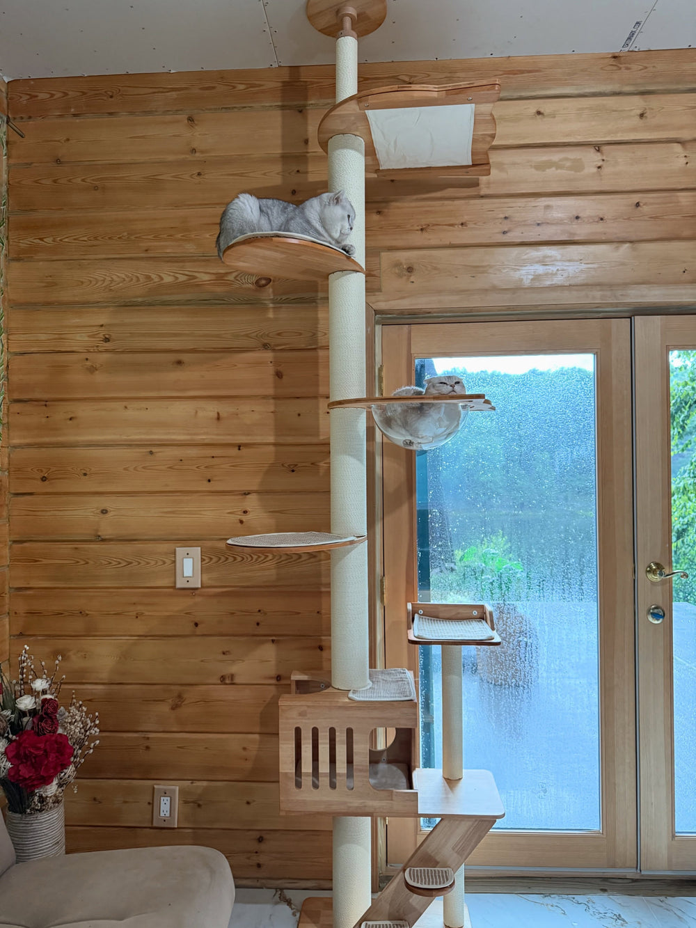 A tall wooden cat tree in a warm wood-paneled living room